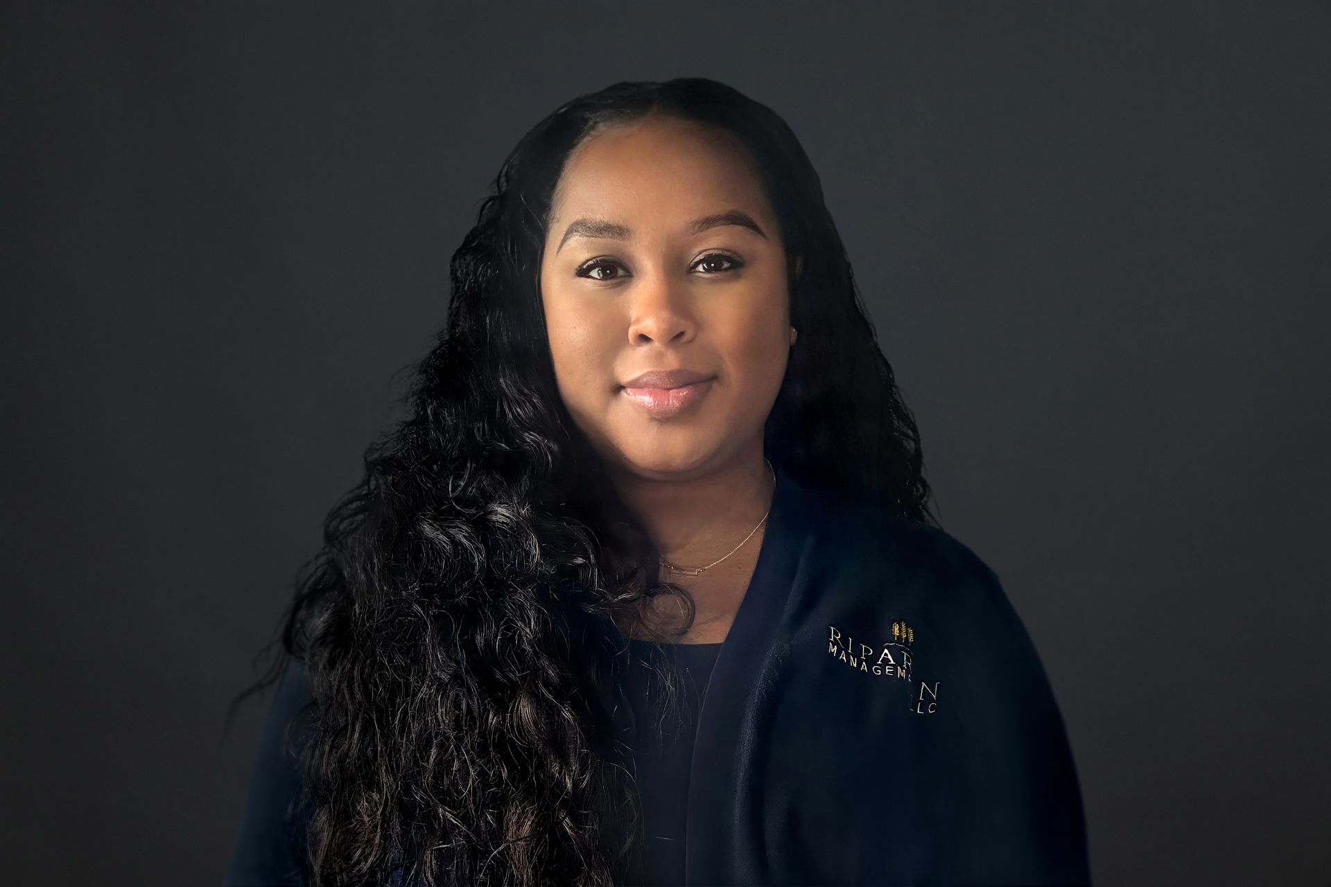 A woman with long curly hair is standing in front of a black background.