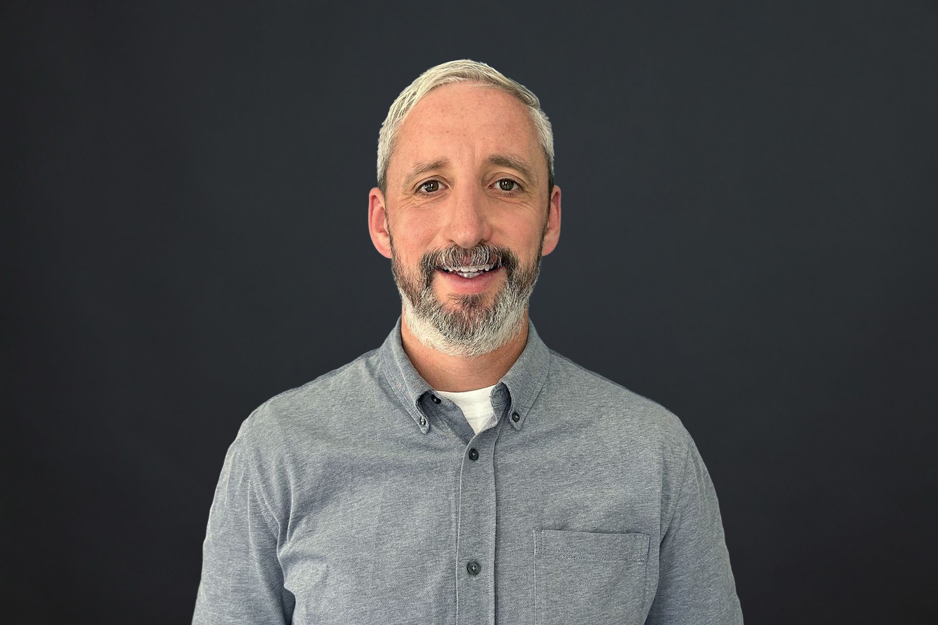 A man with a beard is wearing a blue shirt and smiling.