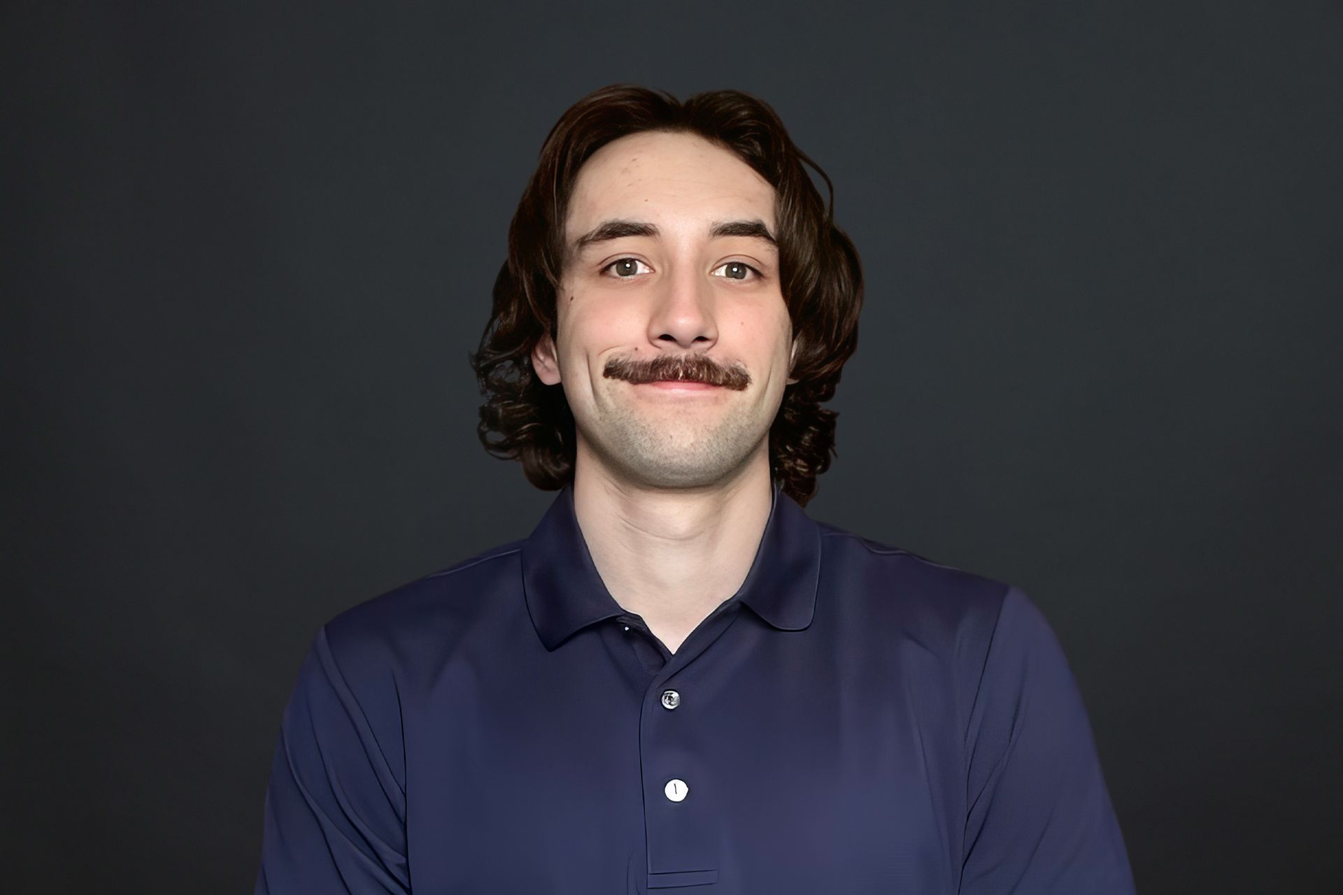A young man with a mustache is wearing a blue shirt and smiling.