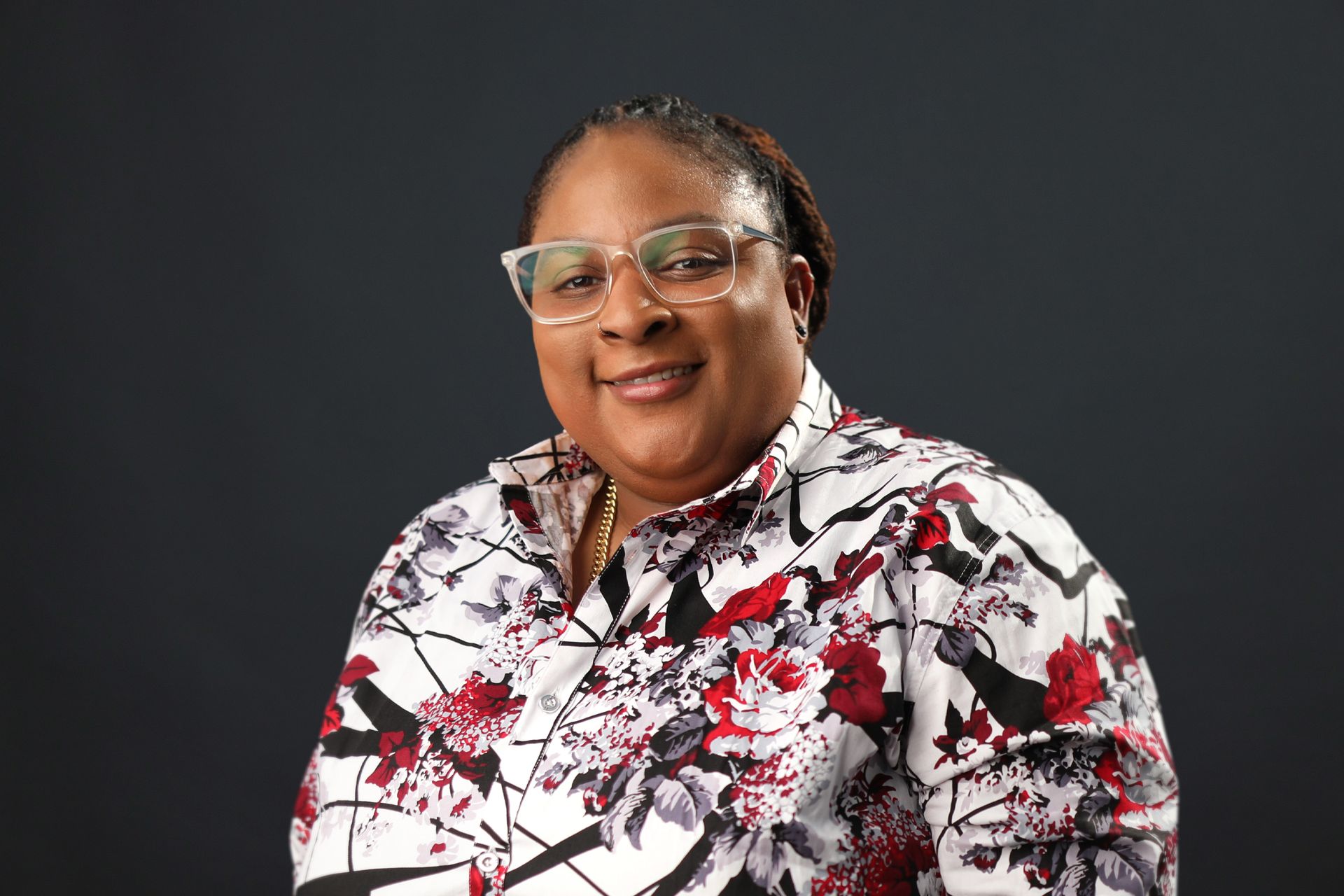 A woman wearing glasses and a floral shirt is smiling for the camera.
