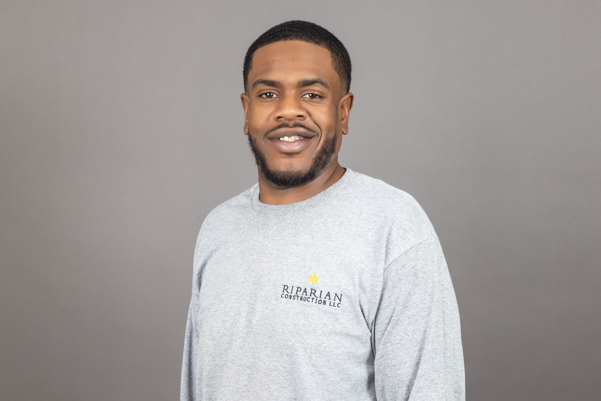 A man with a beard is wearing a grey sweater and smiling.