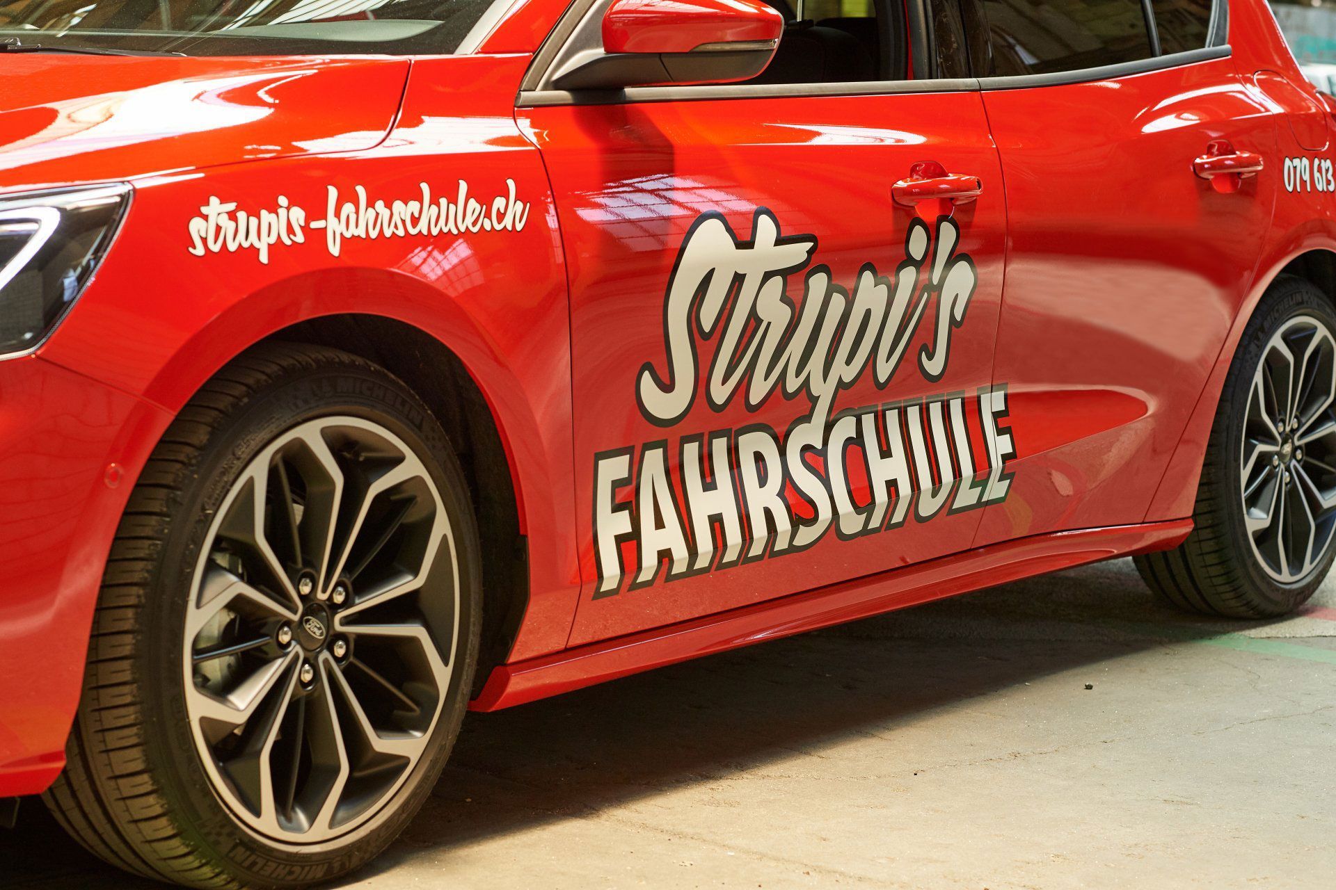 Ein rotes Auto mit der Aufschrift „Strupi's Fahrschule“ auf der Seite