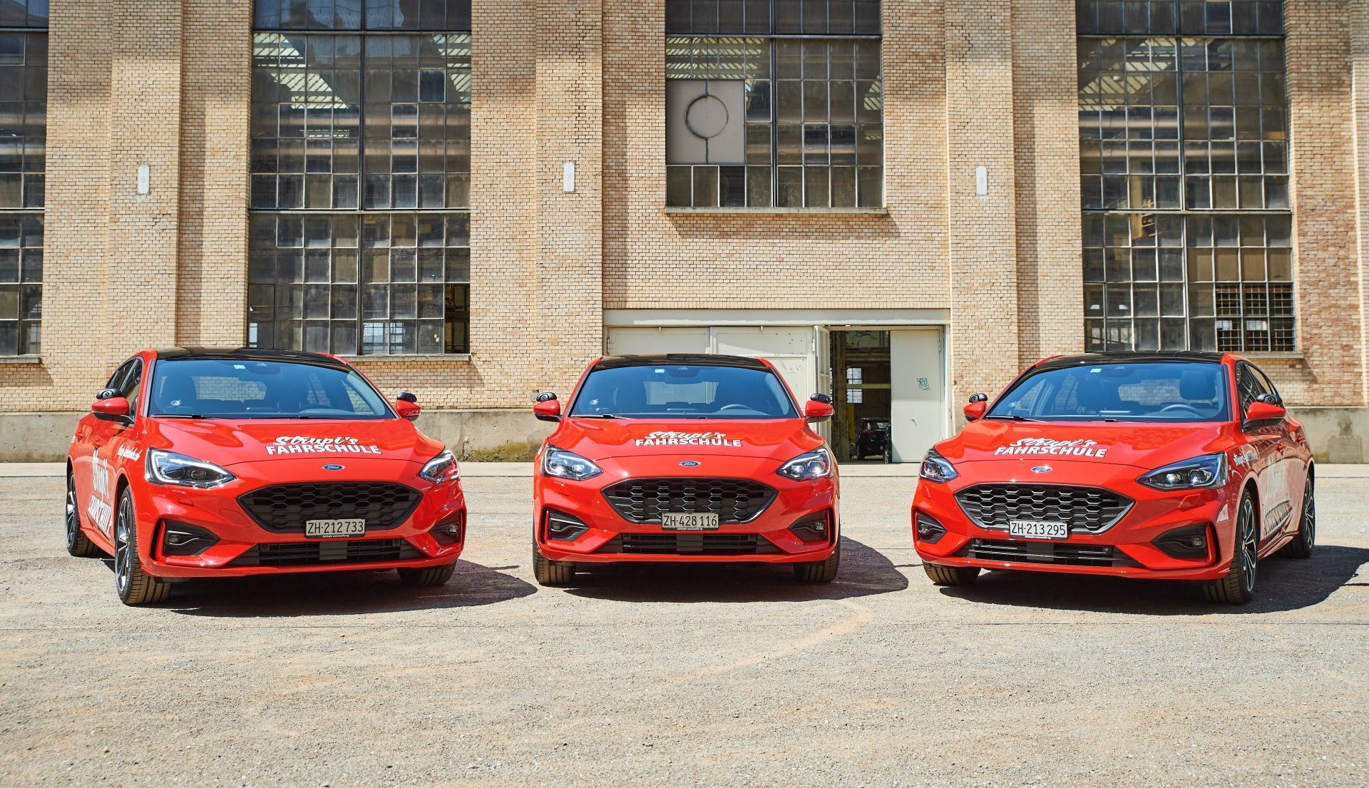 Drei rote Ford Focus-Wagen parken vor einem Backsteingebäude.