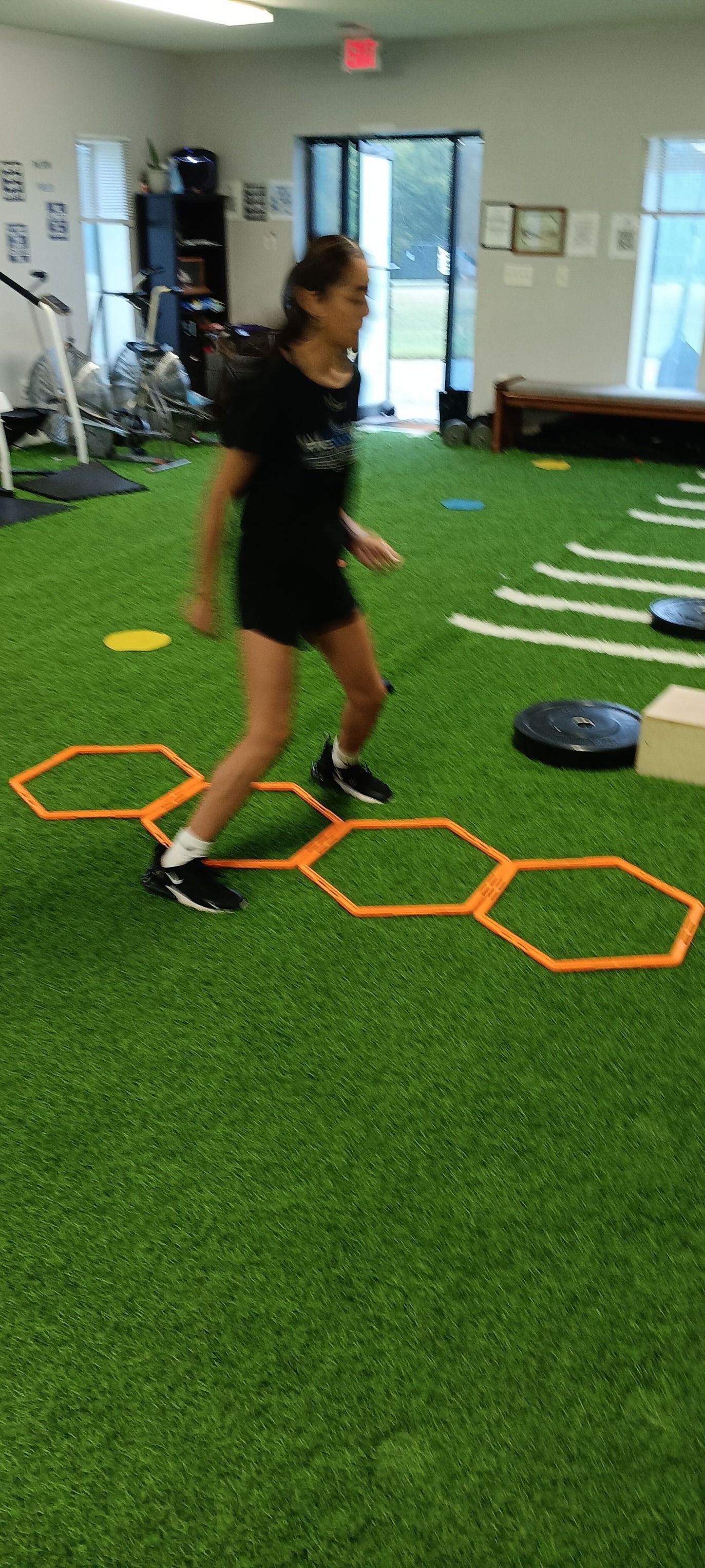 A person performs agility training exercises on artificial turf using orange hexagonal floor hoops.