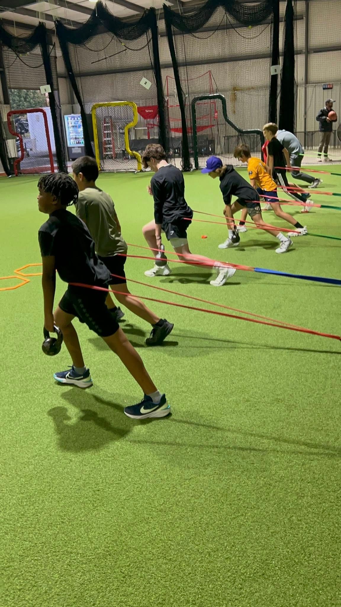 A group of athletes performs split squats with dumbbells in an indoor turf facility.