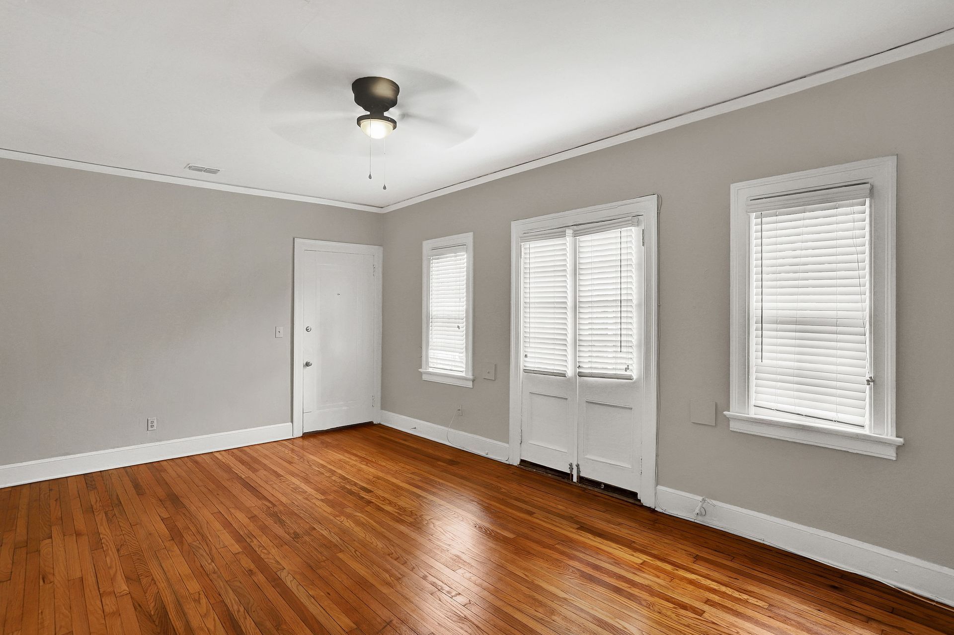 Empty room with hardwood floors, gray walls, white trim, and windows.