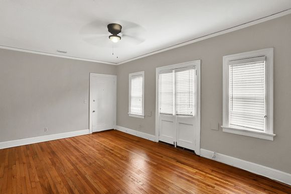 Empty room with hardwood floors, gray walls, white trim, and windows.