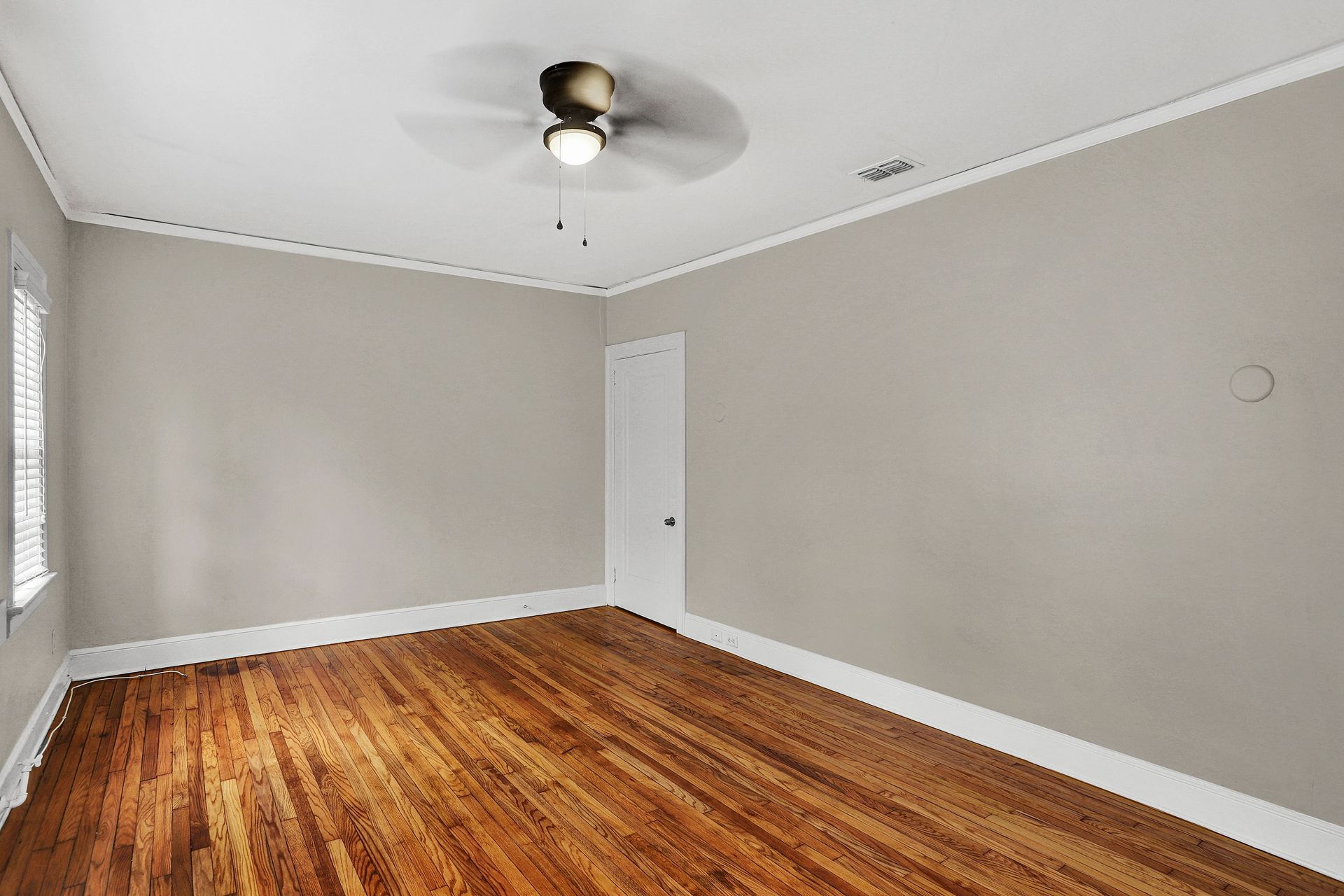 Empty room with wood floor, beige walls, white trim, and a ceiling fan.