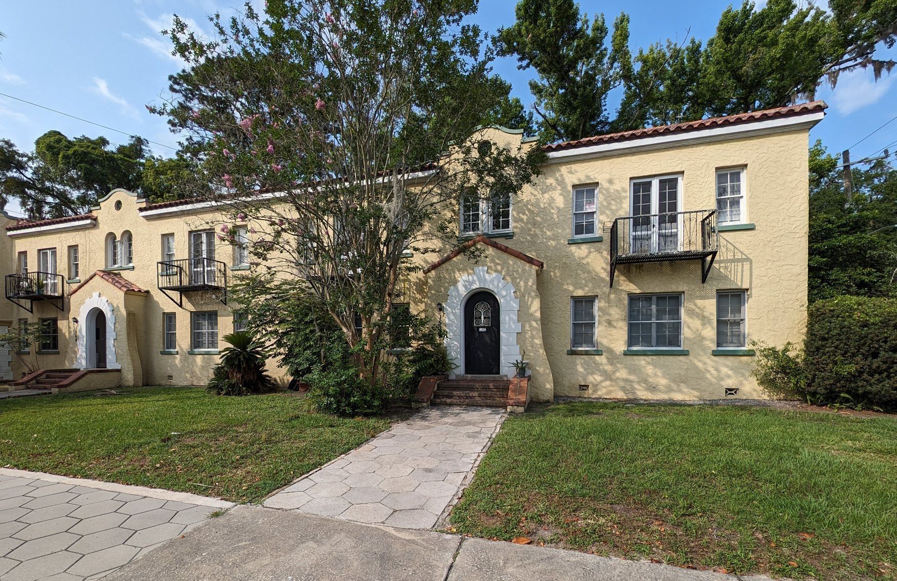 Yellow stucco apartment building with arched doorways and wrought-iron balconies.