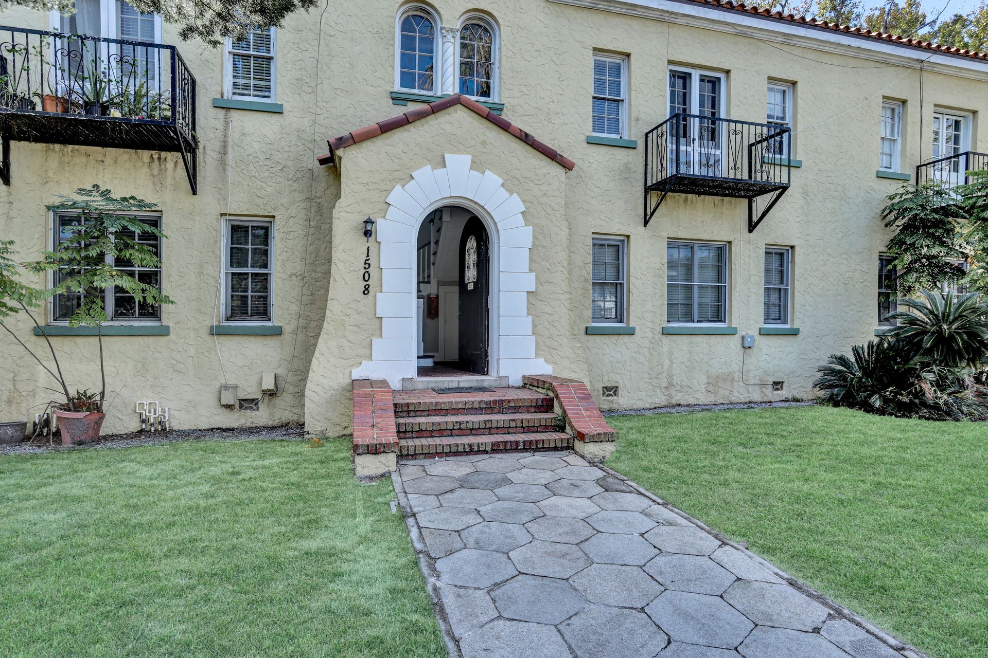 Yellow stucco apartment building with a brick pathway and arched entryway.