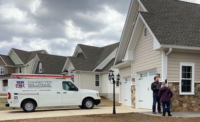 White van parked near a house with people talking; cloudy sky.