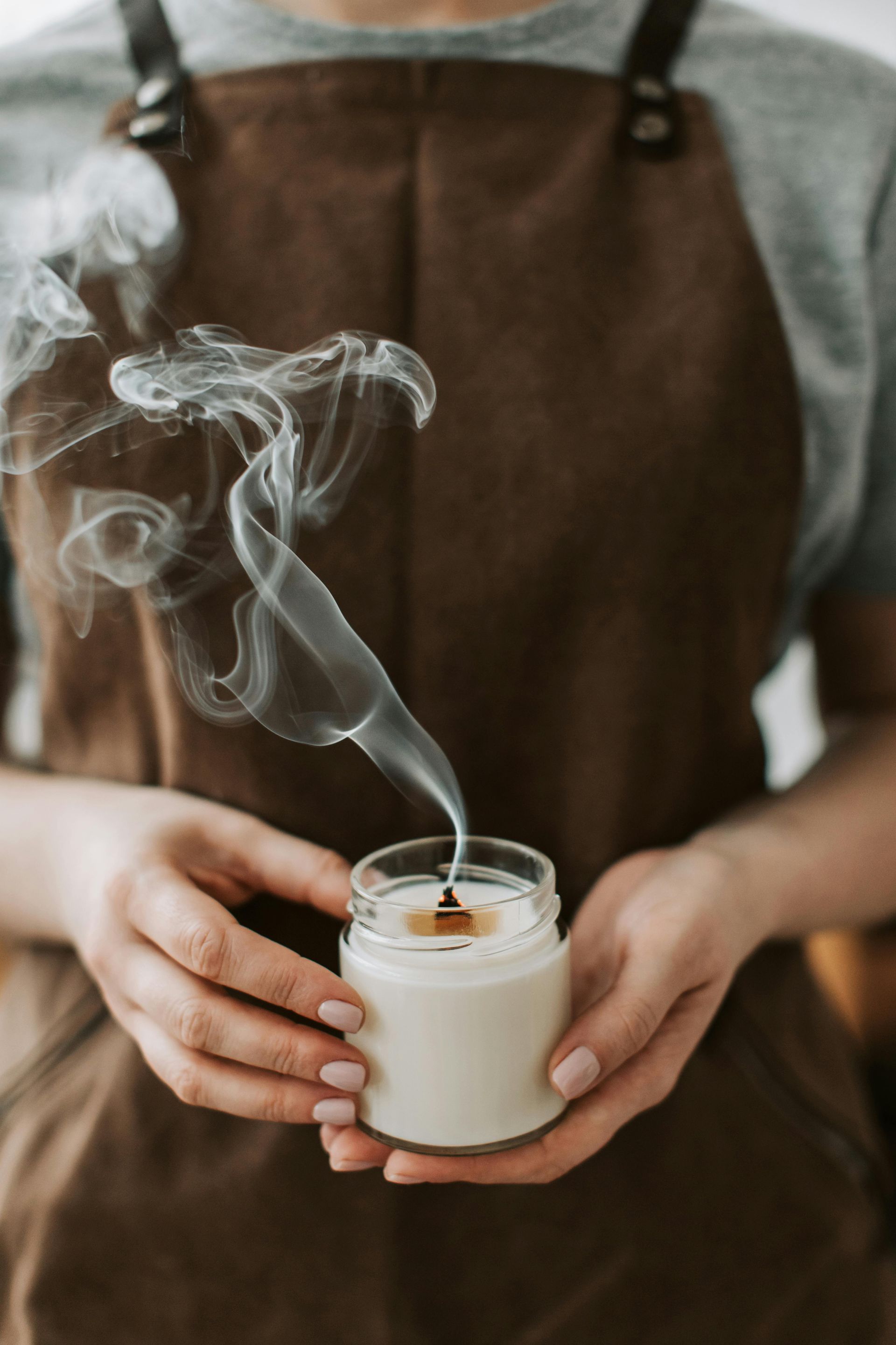 Person holding a recently extinguished candle, smoke rising, wearing a brown apron.