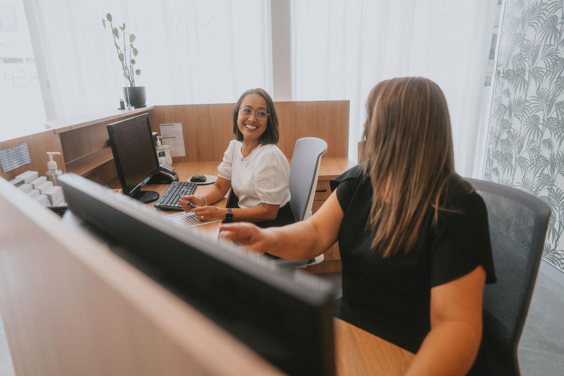 Two Smiling People Working at a Reception Desk — New Leaf Dentists In Erina, NSW