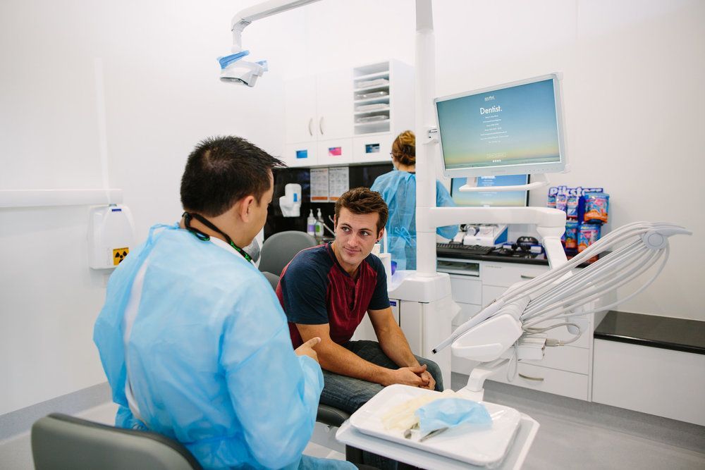Dentist in Blue Gown Consults With Patient in a Dental Office — New Leaf Dentists in Erina, NSW