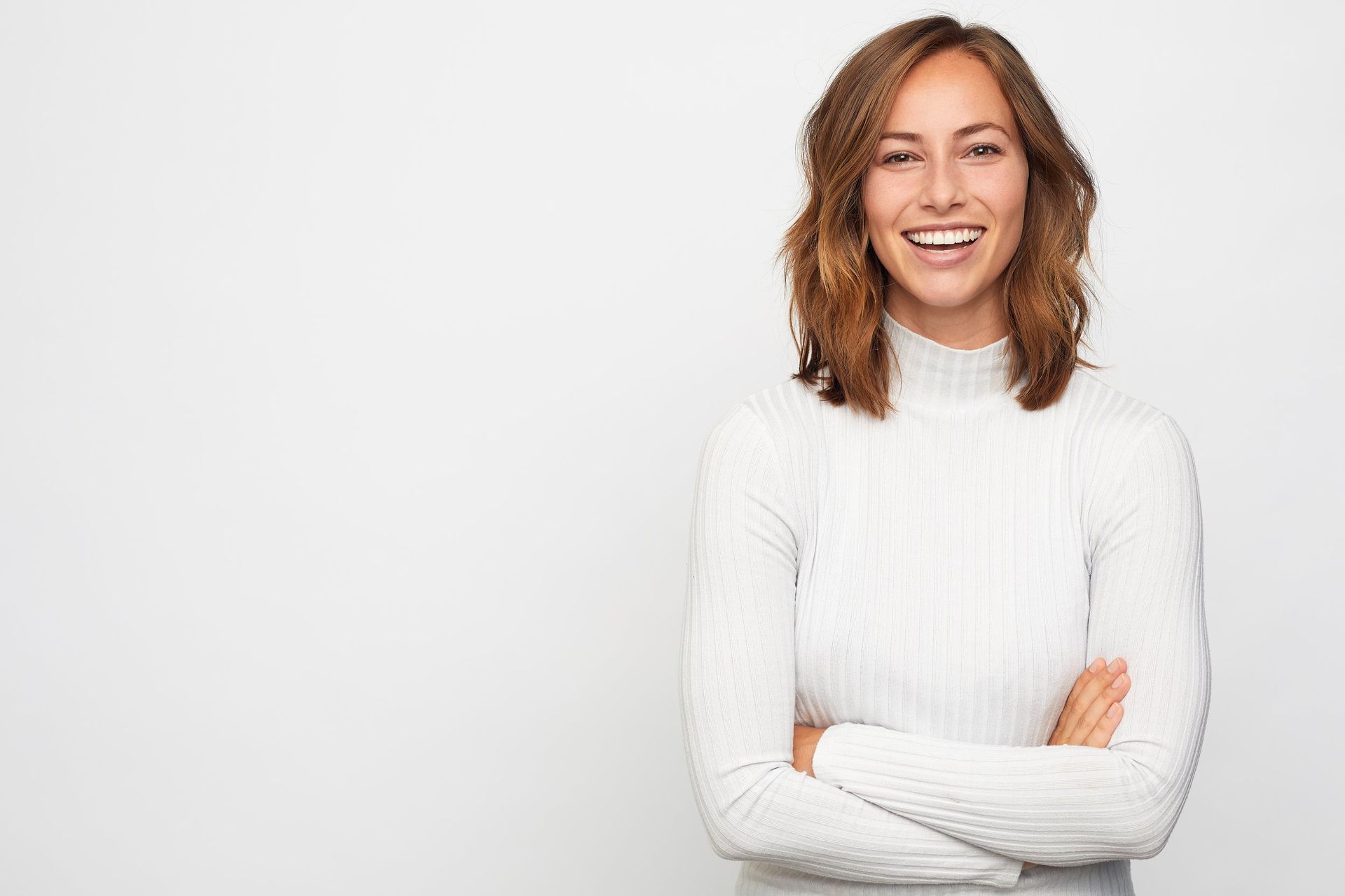 A Woman in a White Sweater is Smiling With Her Arms Crossed — New Leaf Dentists in Erina, NSW