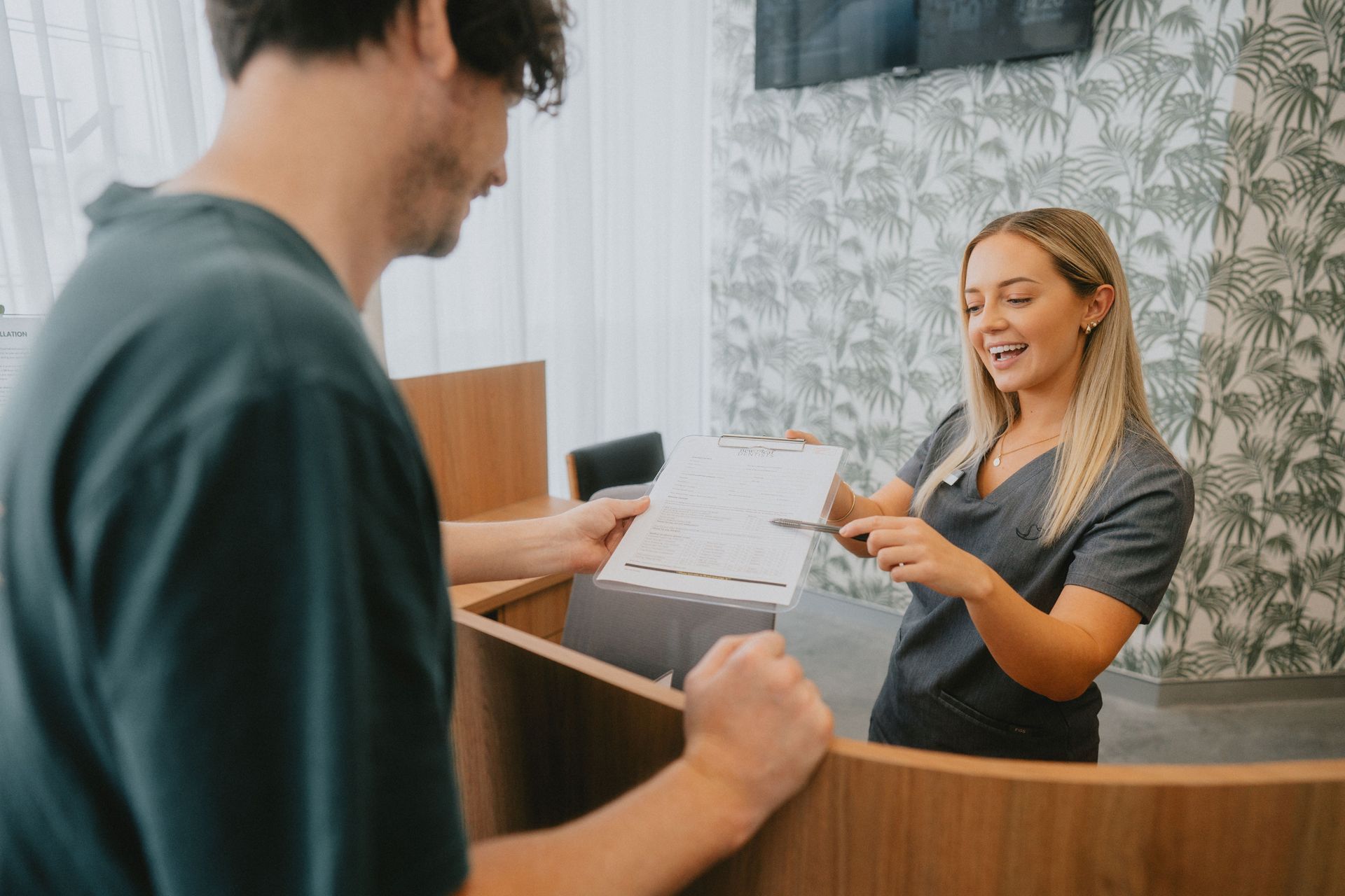Blond Receptionist in Grey Scrubs Shows Paperwork — New Leaf Dentists In Erina, NSW