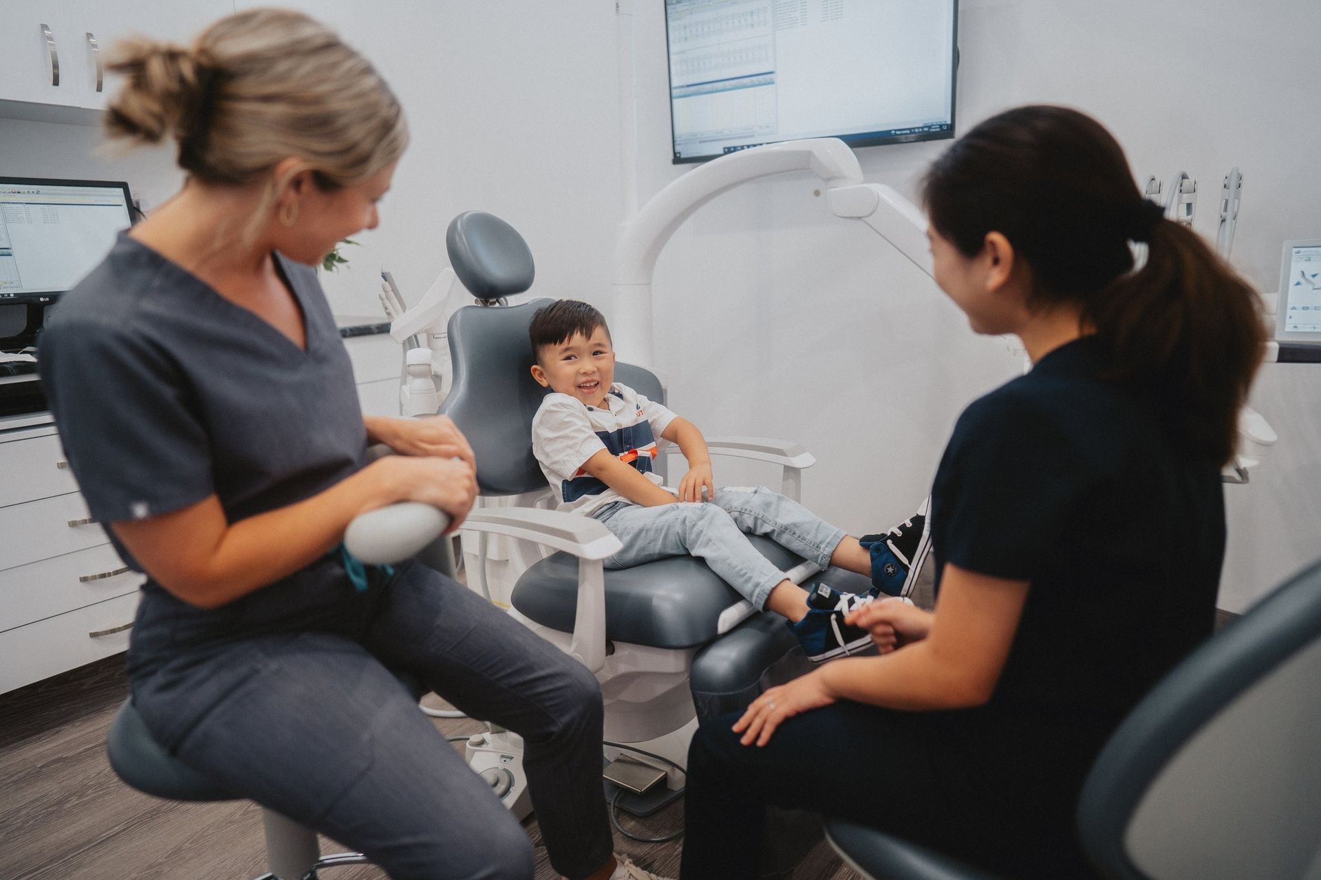 A Little Boy is Sitting in a Dental Chair Talking to Two Women — New Leaf Dentists in Erina, NSW