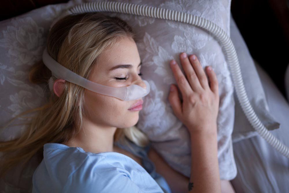 A Woman is Sleeping in a Bed With an Oxygen Mask on Her Face — New Leaf Dentists in Erina, NSW