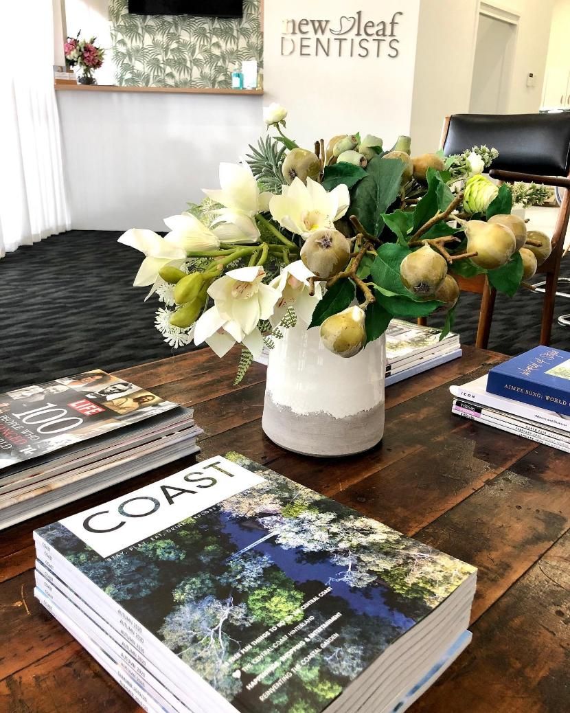 A Vase of Flowers is Sitting on a Wooden Table Next to a Stack of Books — New Leaf Dentists in Erina, NSW