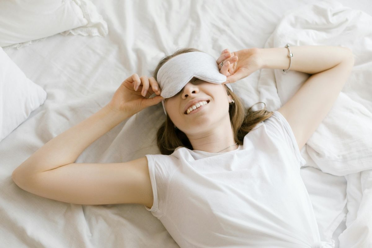A Woman is Laying in Bed With a Sleep Mask on Her Eyes — New Leaf Dentists in Erina, NSW