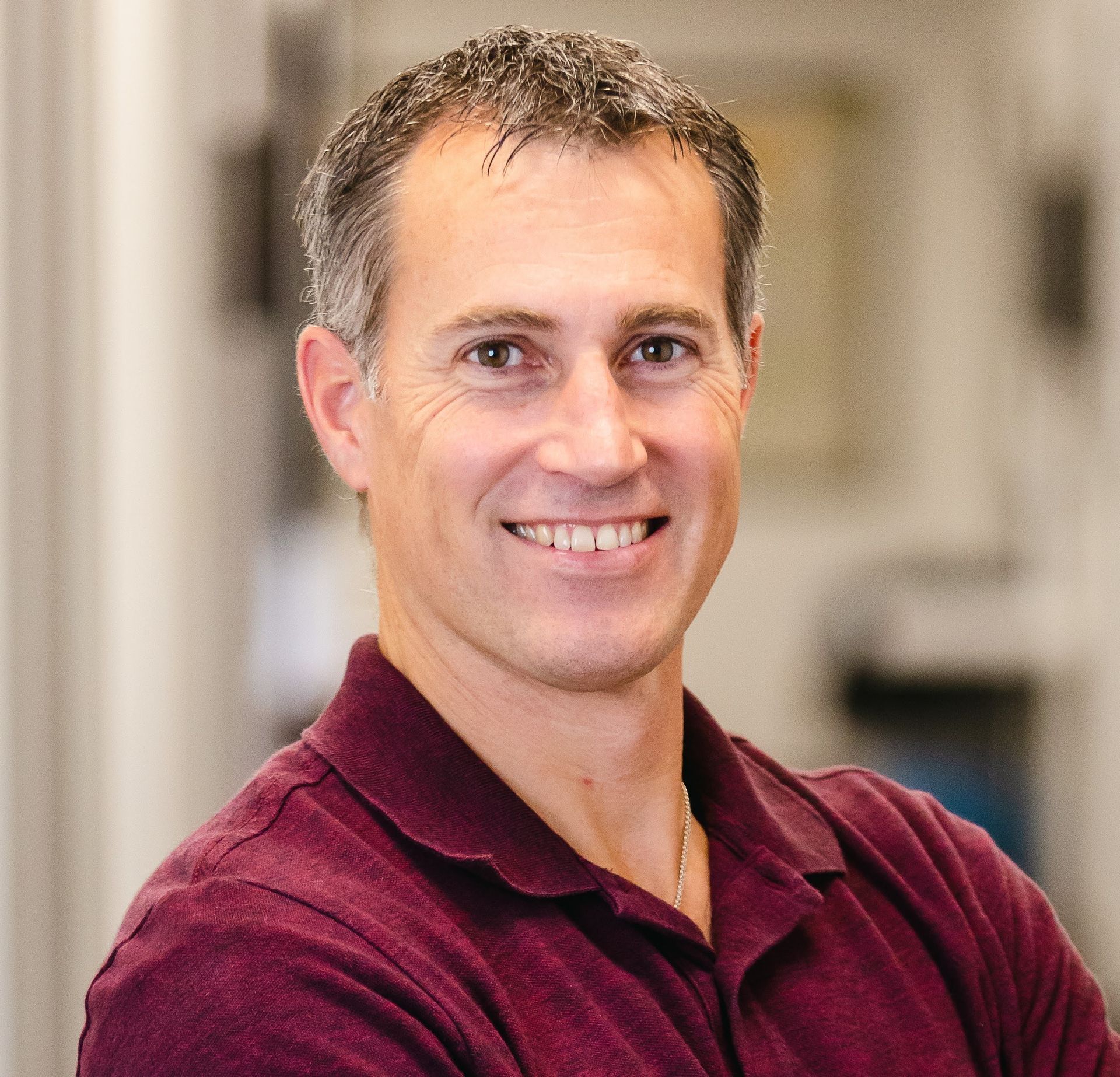 A woman wearing glasses and a gray jacket is smiling on the beach.