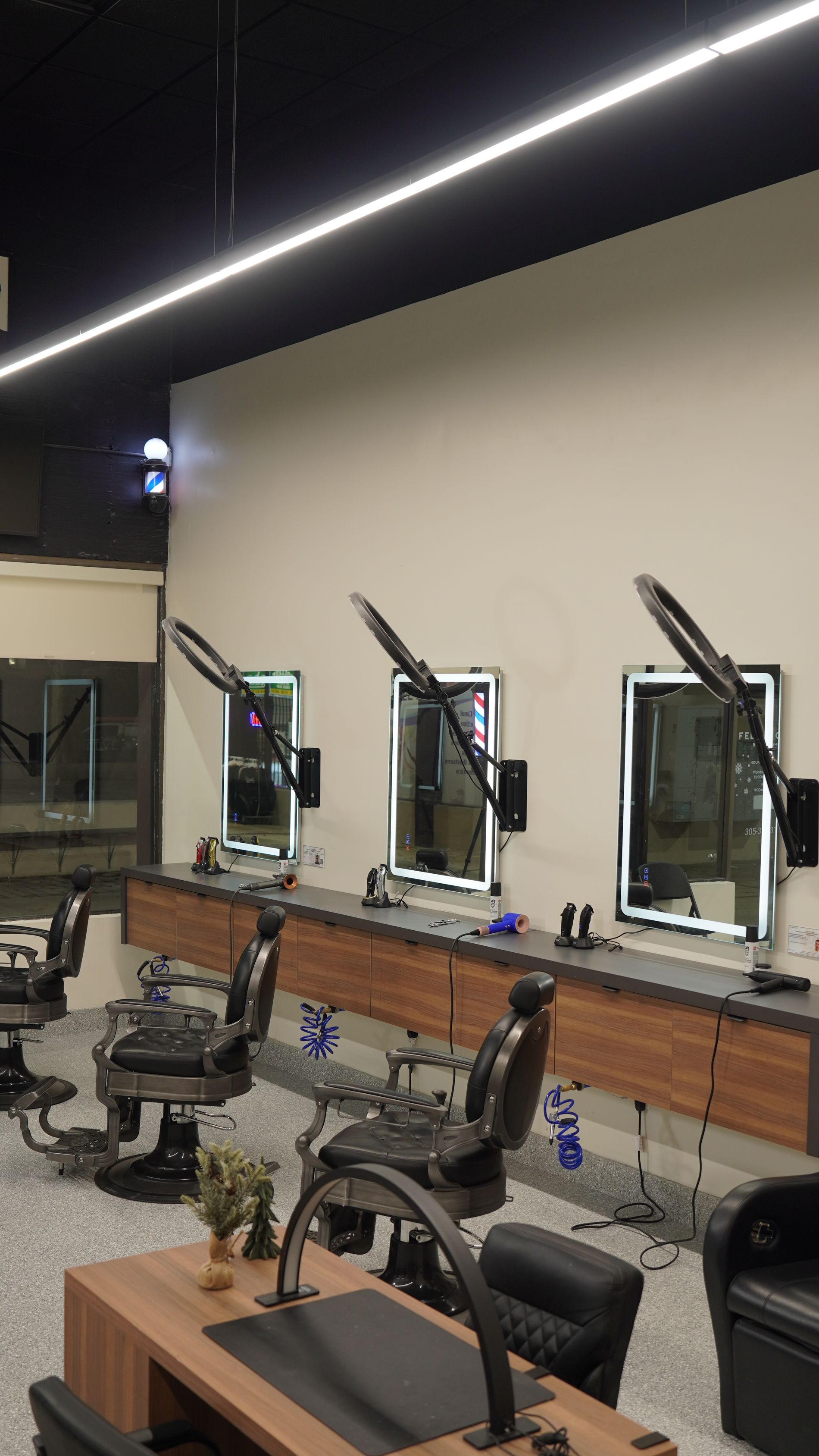 Barbershop interior with mirrors, chairs, and lighting along the wall.