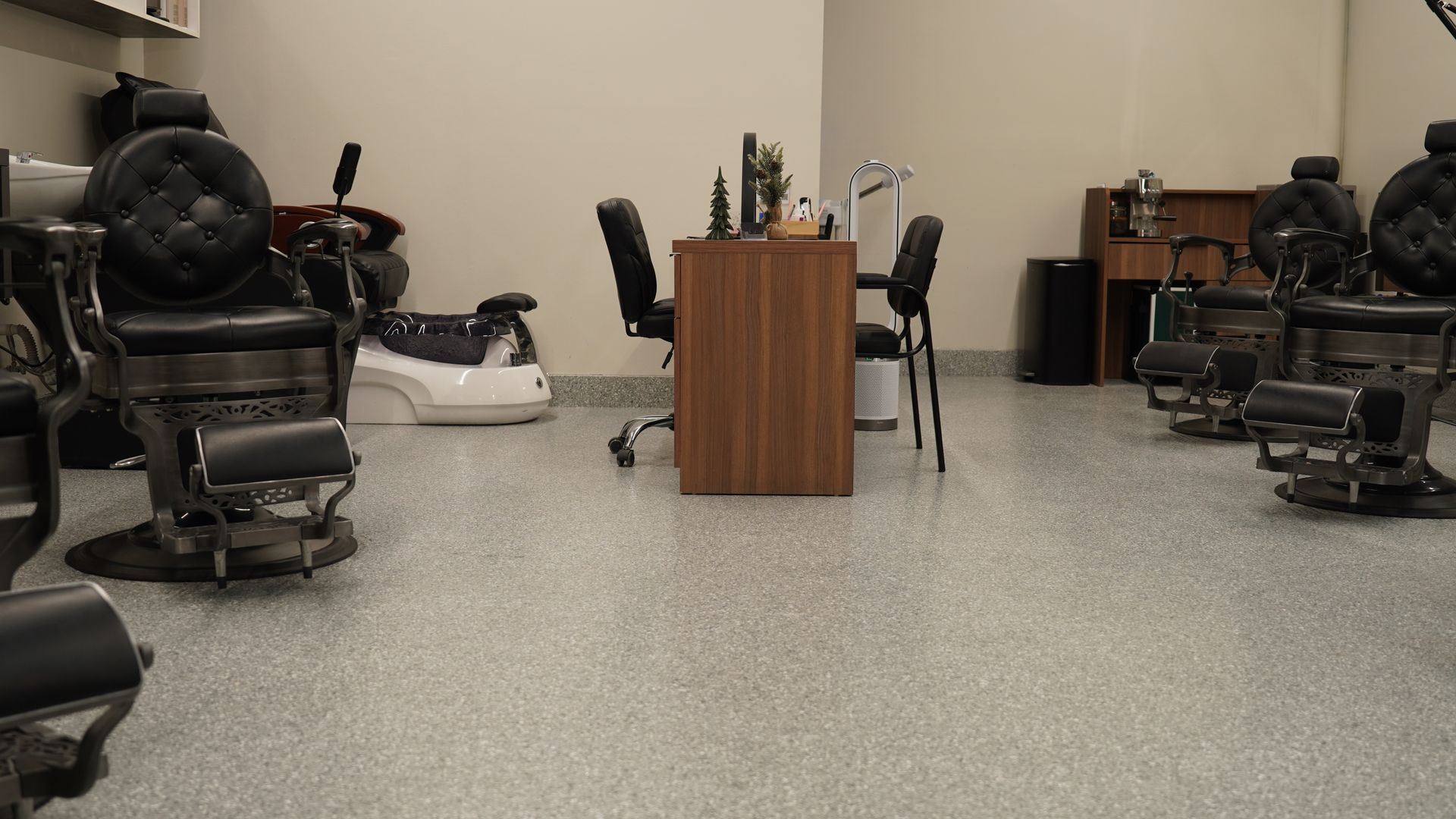Barbershop interior with several black barber chairs, a small table, and a light-colored speckled floor.