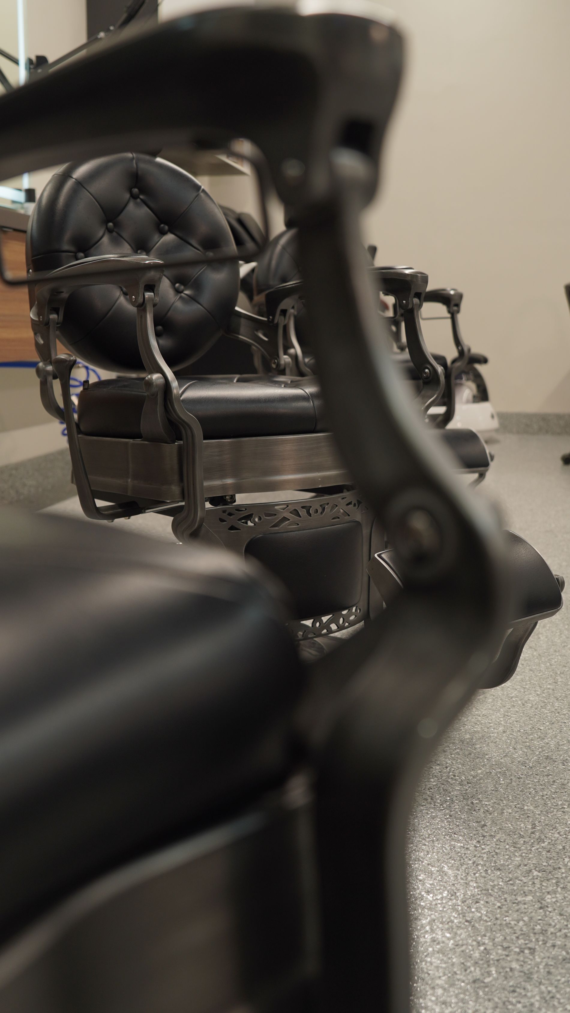 Antique barber chairs in a barbershop. Black leather seats, metal frames, and a light-colored floor.
