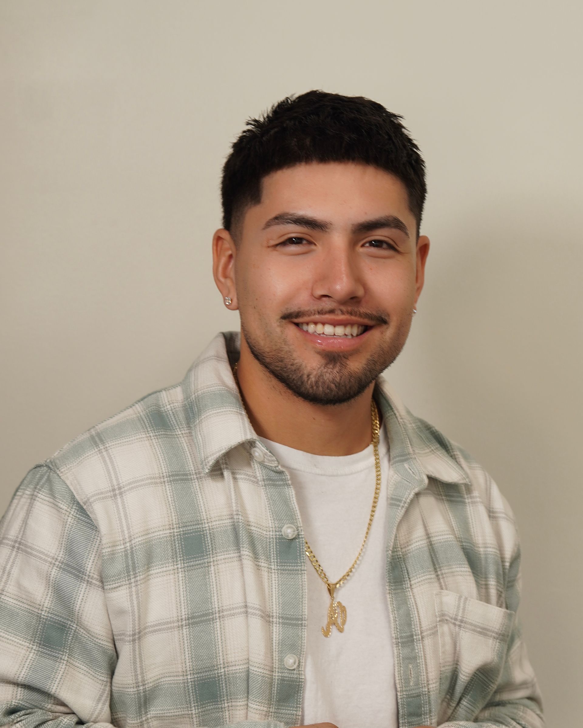 Man with short dark hair, wearing a plaid shirt over a white tee, smiling.