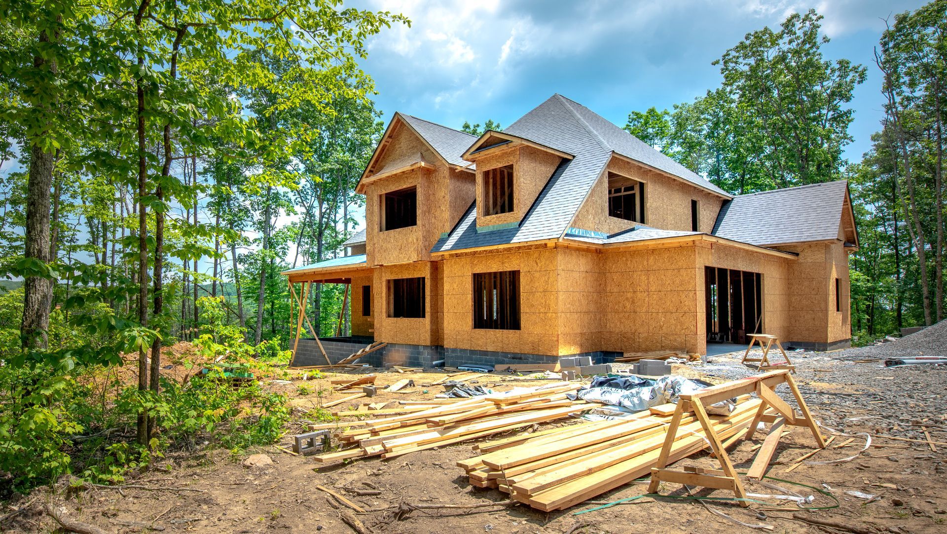 House under construction in a wooded area, with wooden beams and a partially built roof.