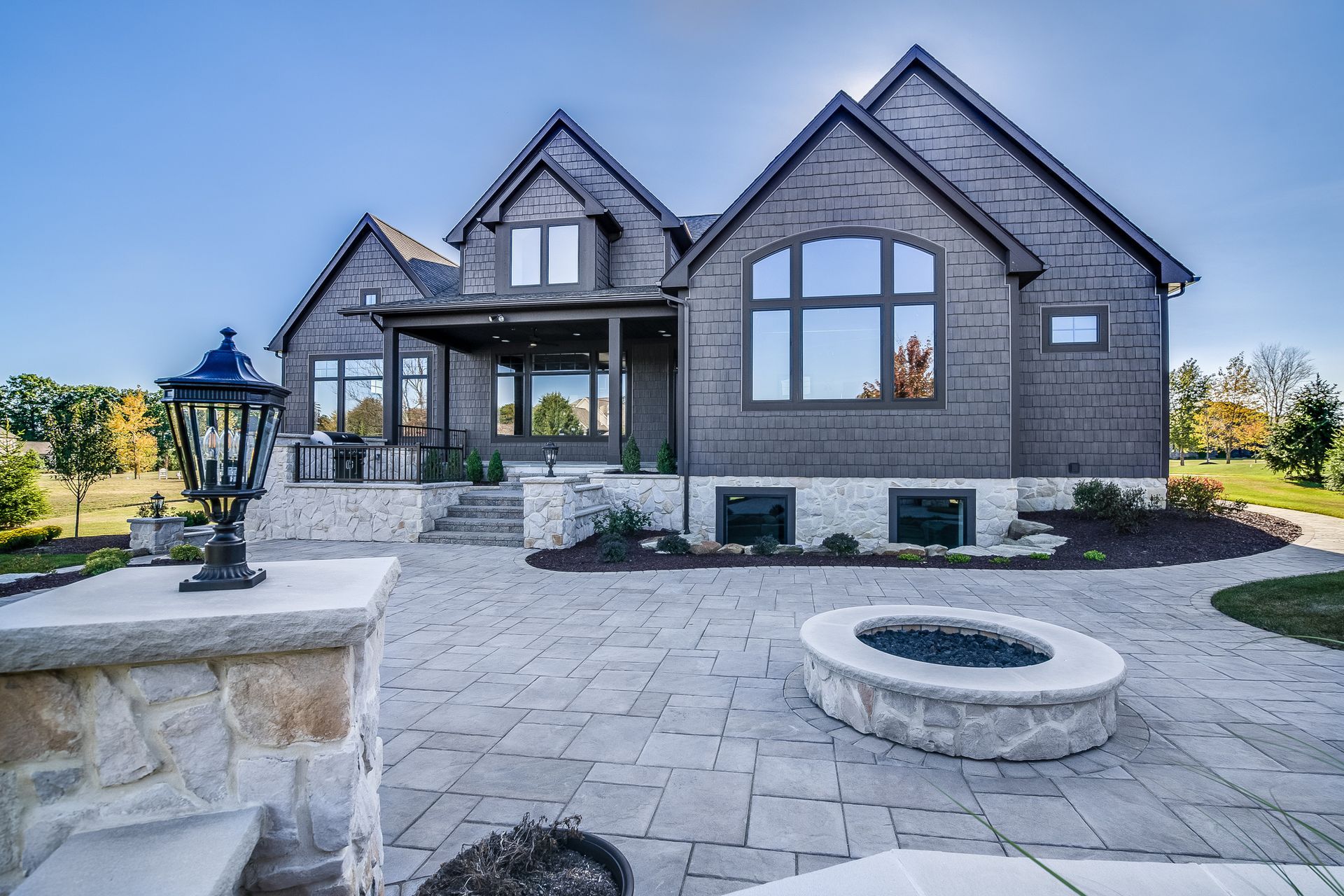 Backyard patio of a modern home with stone pavers, fire pit, and a decorative lamp.