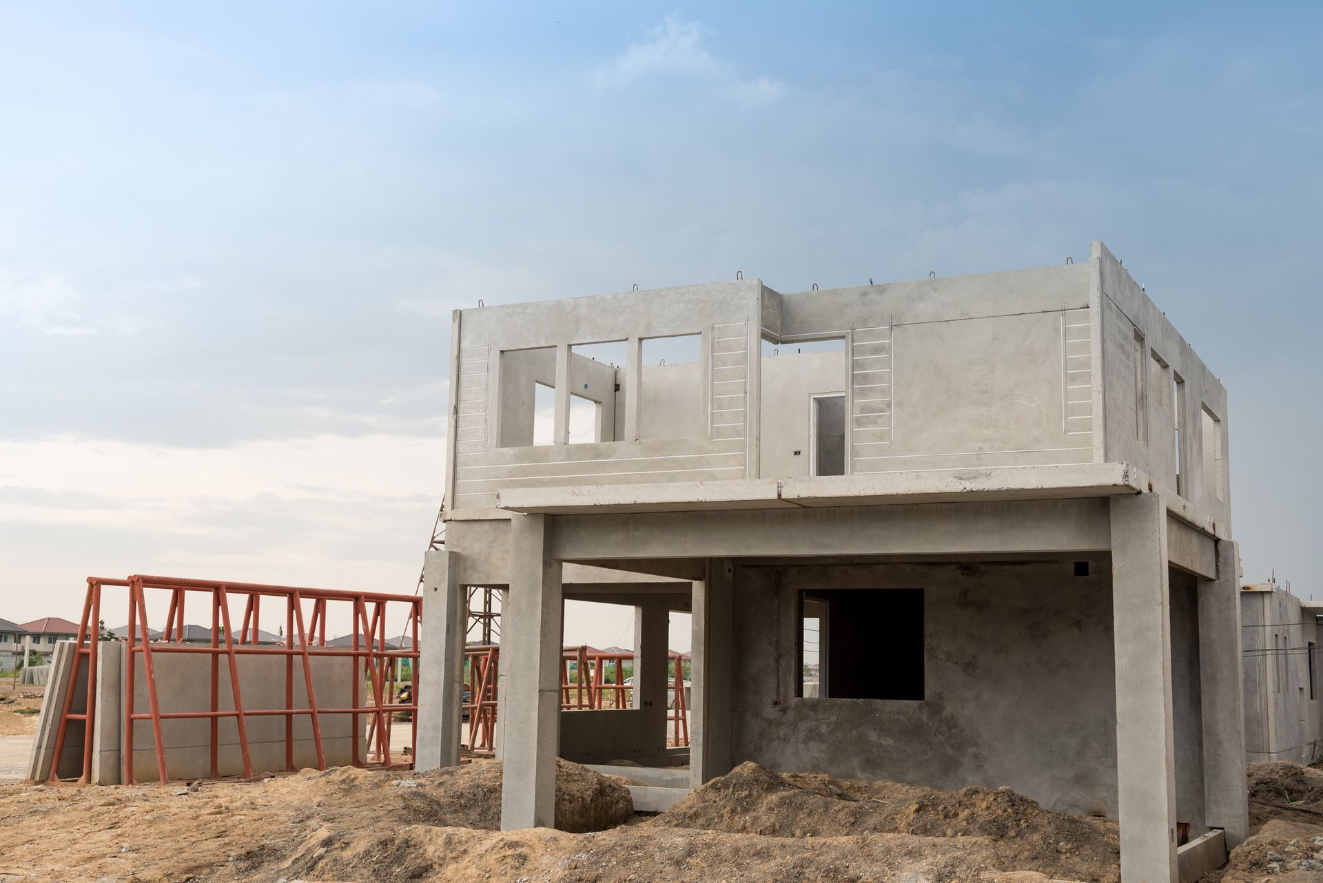Concrete shell of a house under construction on a dirt lot, against a blue sky.