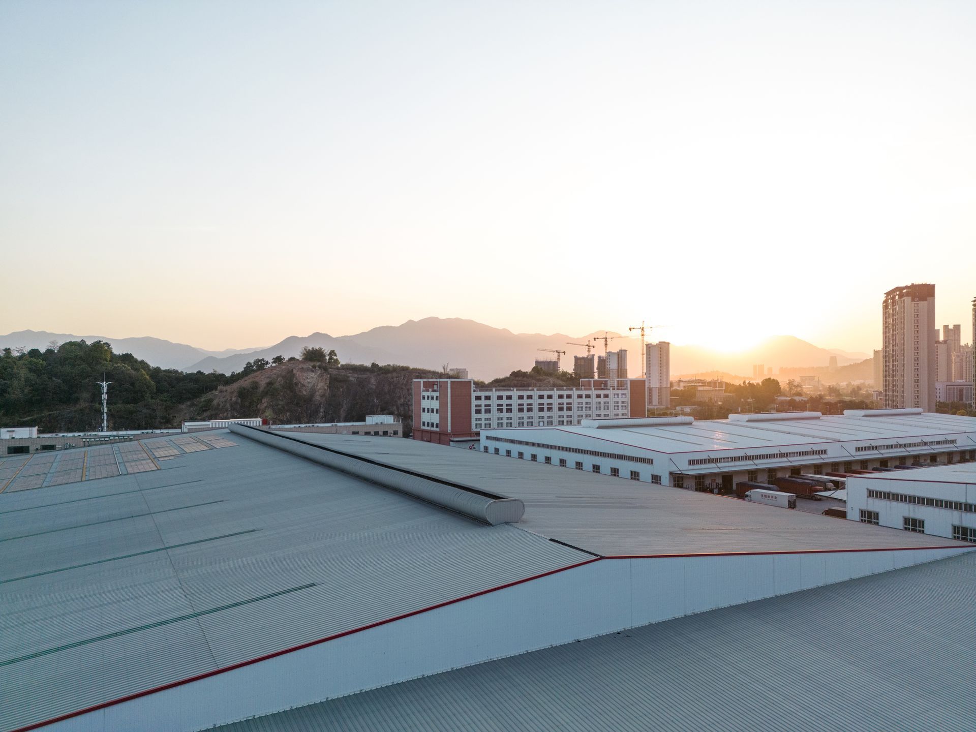 Rooftop view of industrial buildings with mountain backdrop and golden sunrise.