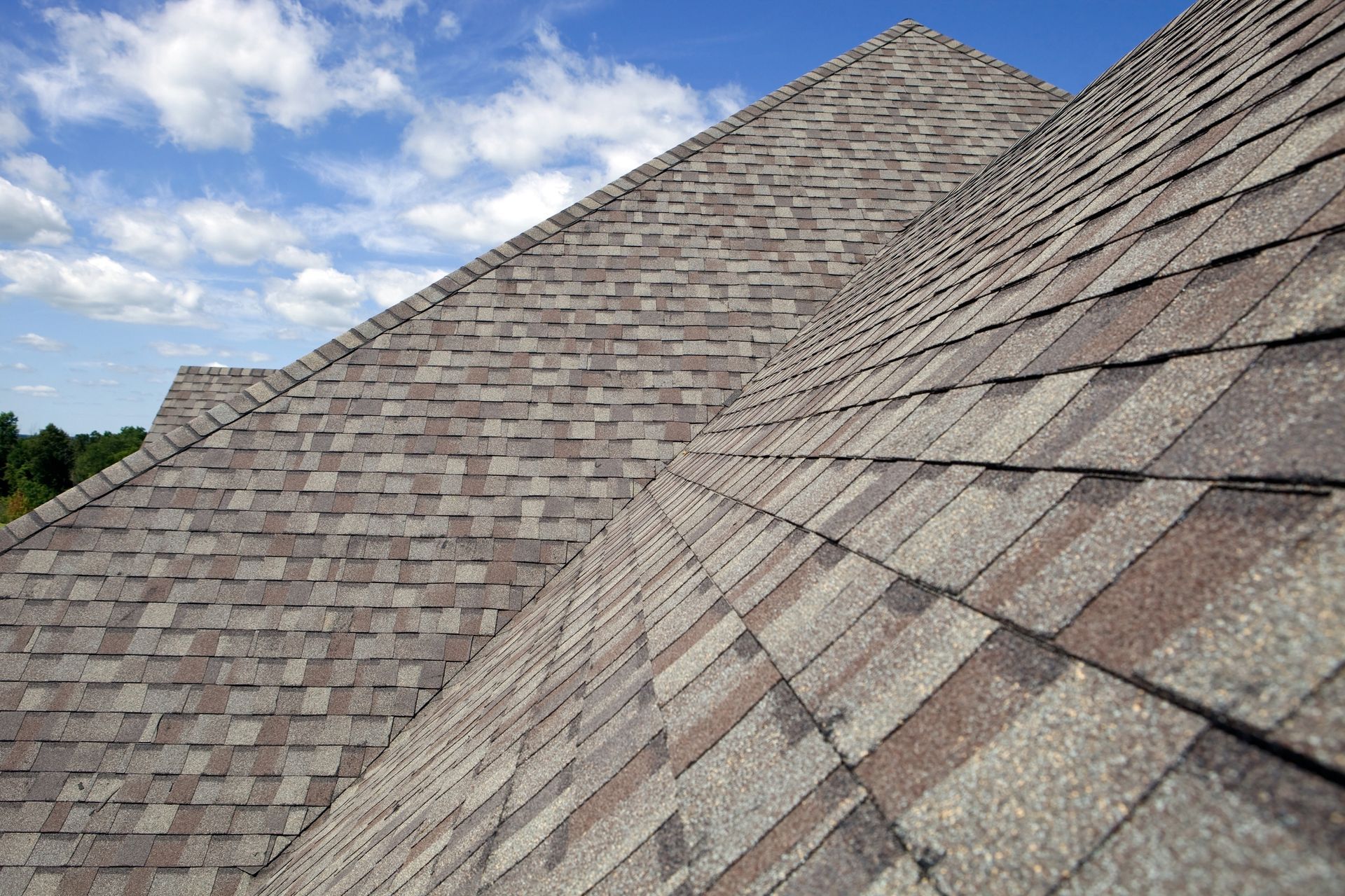 Close-up of a shingled roof against a blue sky with fluffy clouds.