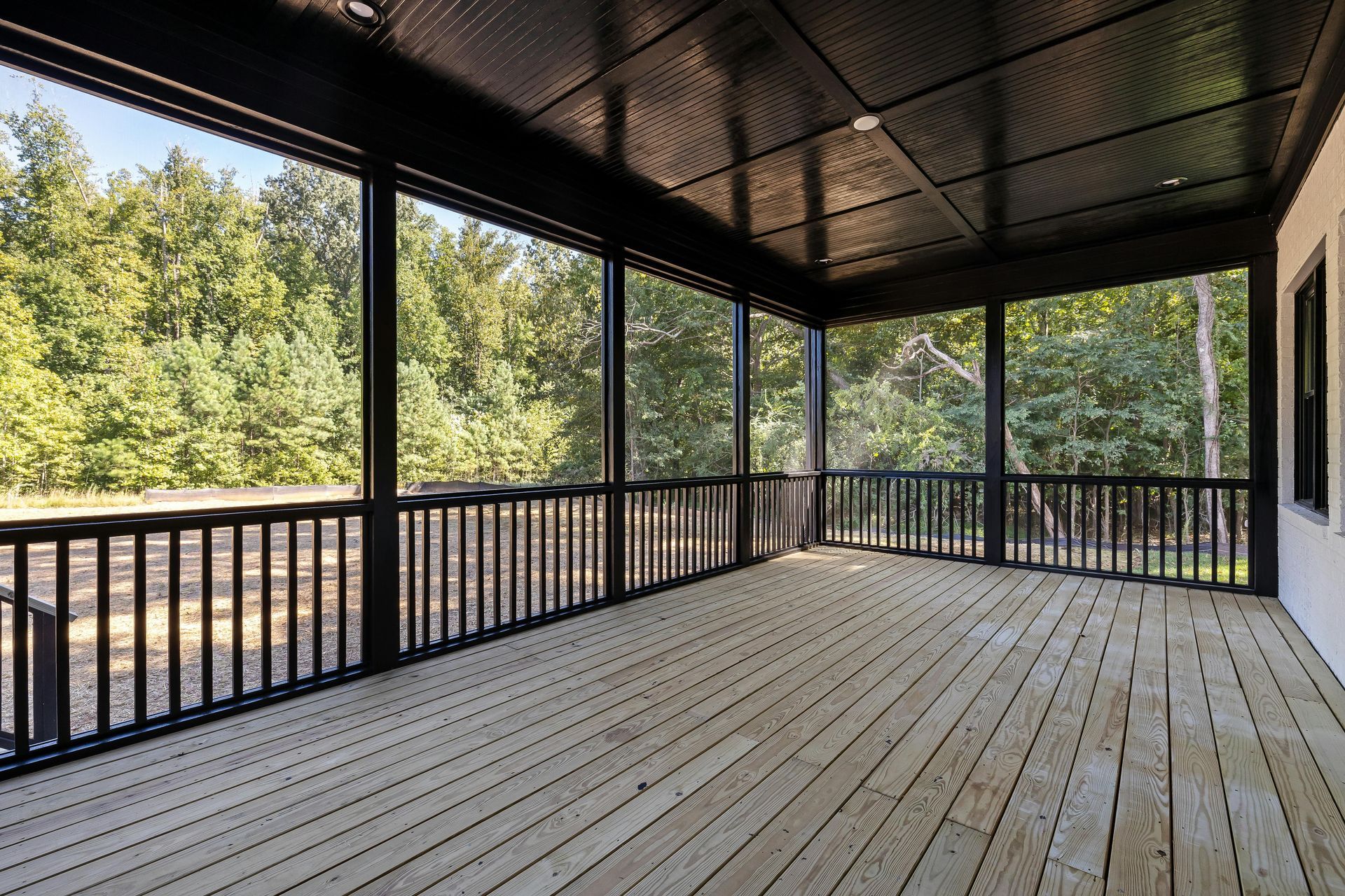 An empty screened in porch with a wooden deck and trees in the background.