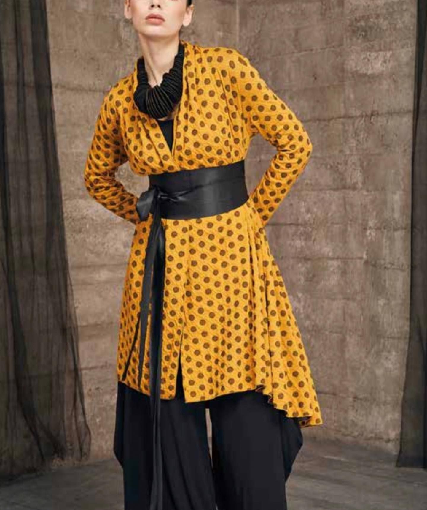 Woman in yellow polka dot jacket and black pants, black belt.