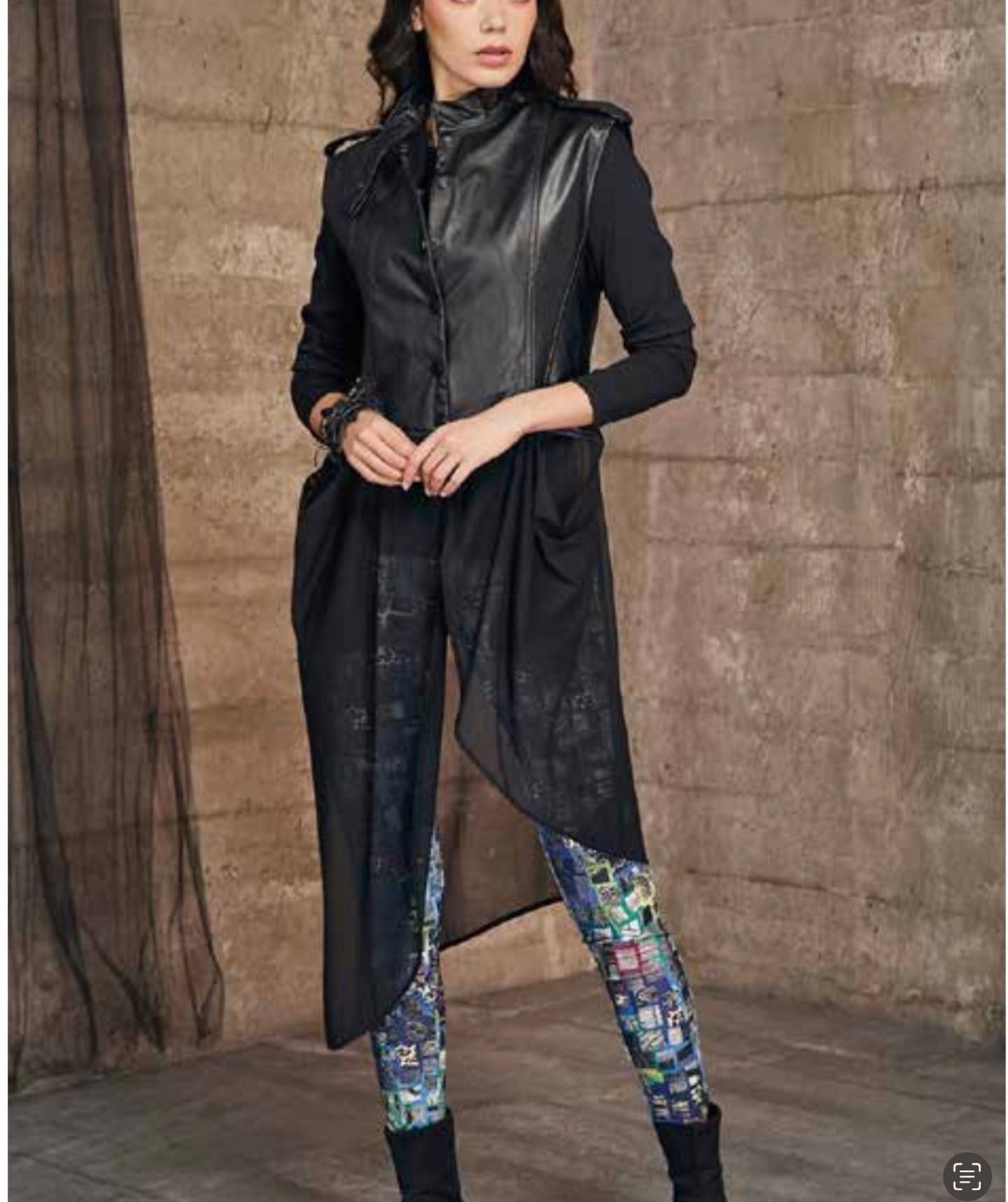 Woman in black outfit and patterned leggings, standing against a textured backdrop.