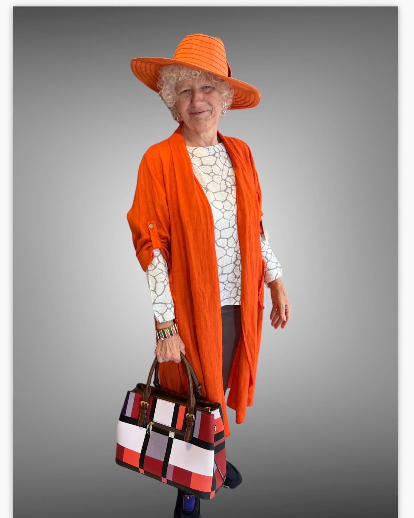 Woman in orange outfit and hat, holding a patterned bag.
