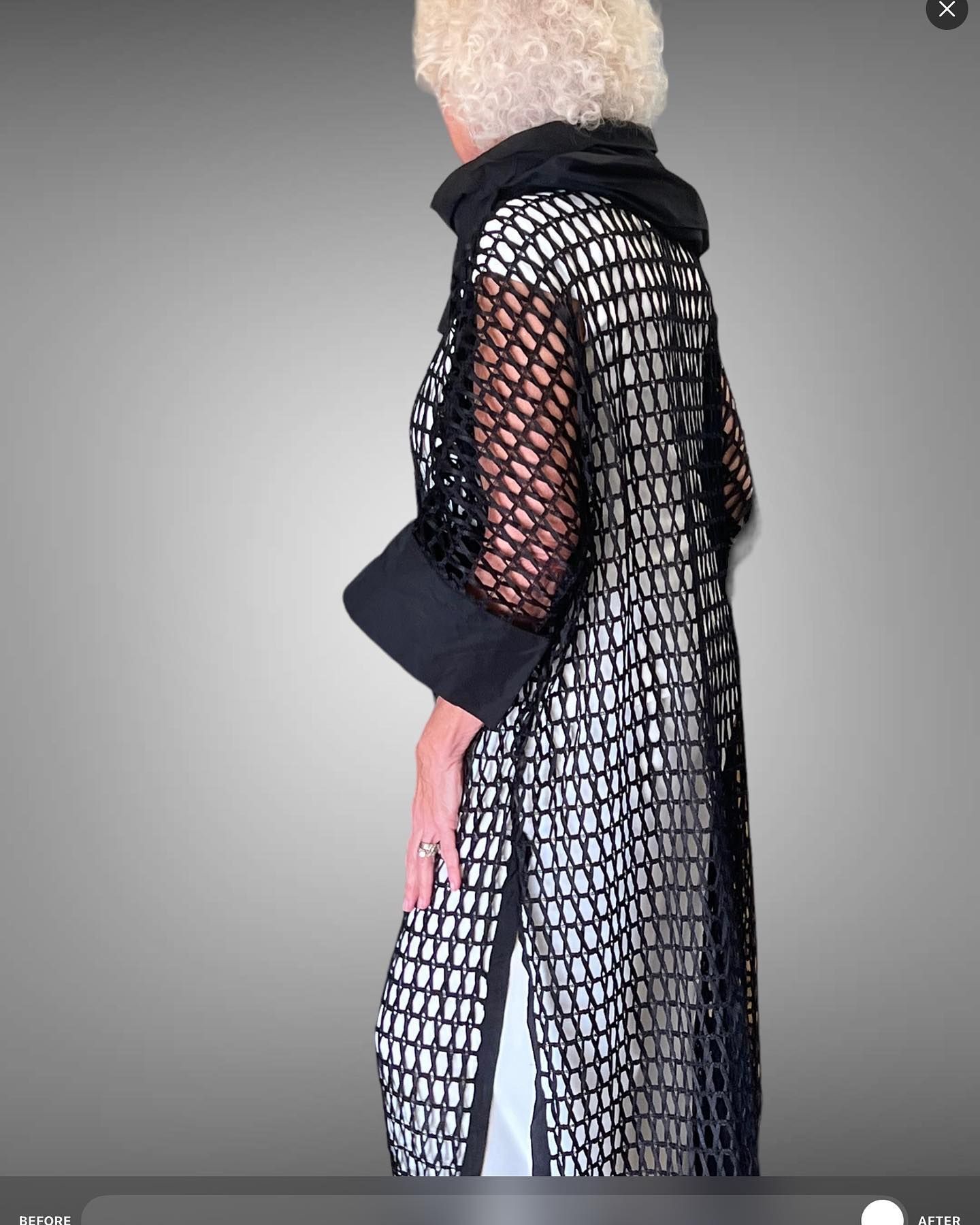 Woman wearing a long black net coat over a white outfit; gray background.