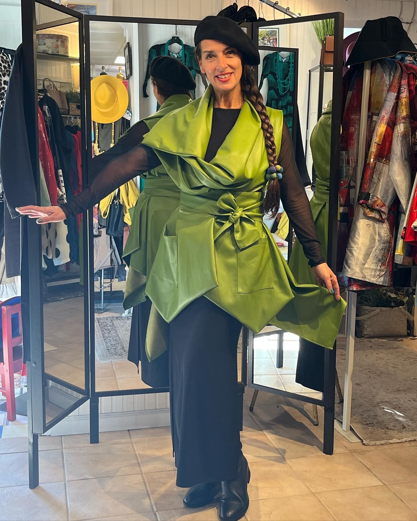 Woman in black dress and lime green wrap, in a shop, smiling.