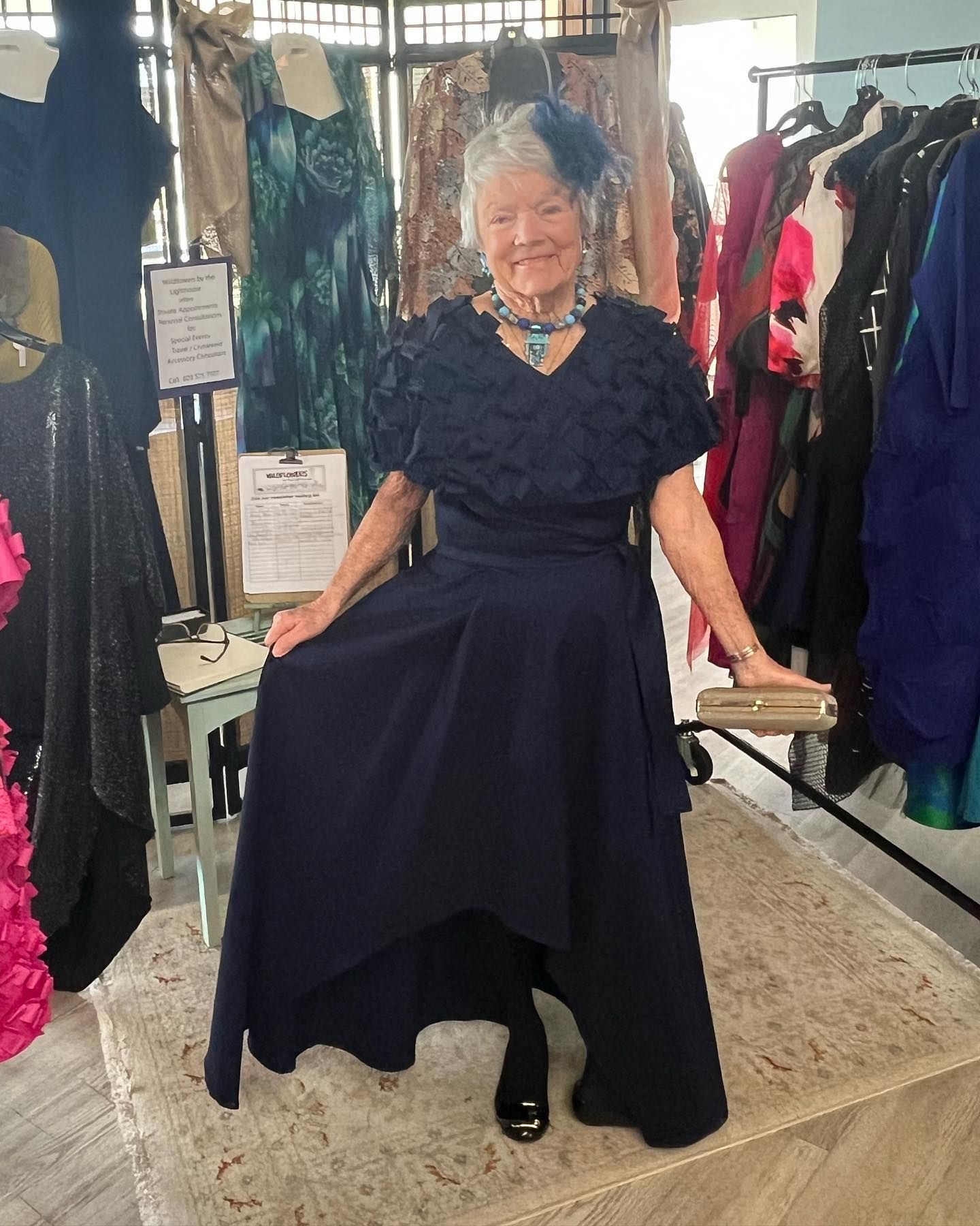 Woman in a dark blue formal dress, posing in a clothing store, smiling.