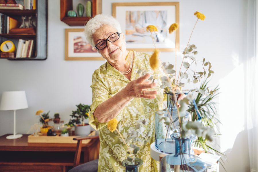 An older woman arranges flowers in her home, where she maintains her independence thanks to the support of home care.
