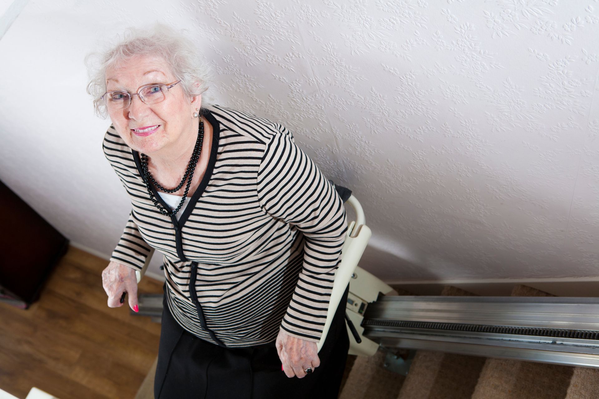  An older woman smiles as she rides a stair lift, one of the home modifications that help her stay s