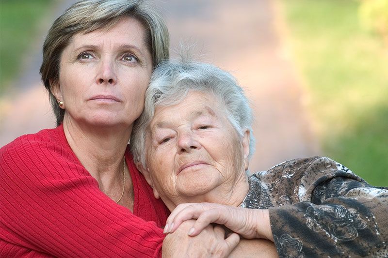 A woman hugs her older mother as she ponders the risk factors of Alzheimer’s disease.