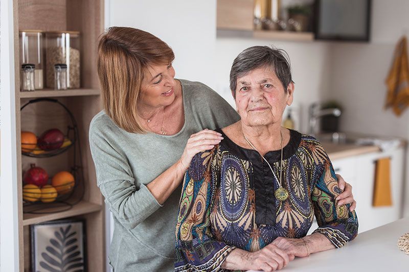An older woman experiencing time-shifting in dementia stares forward as her caregiving places her arms around her.