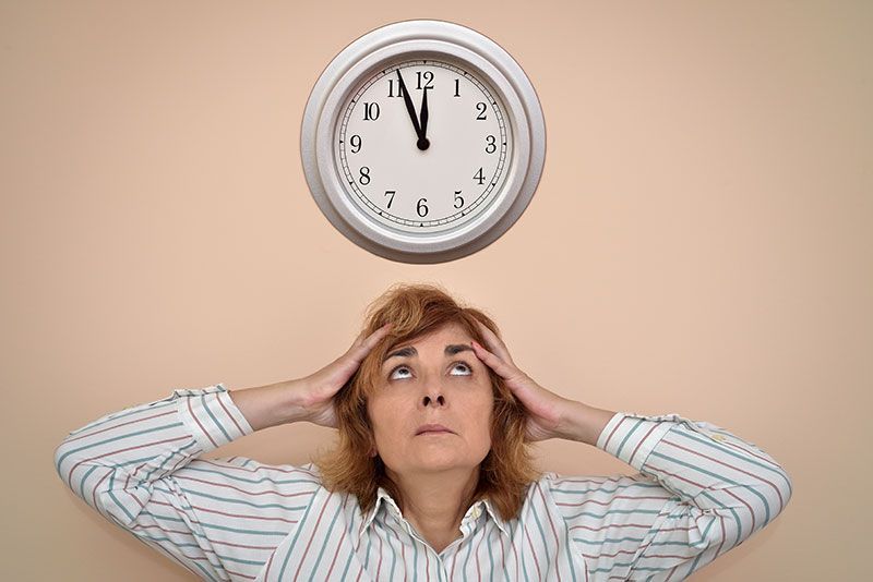 A woman looks flustered as she stands beneath a clock, preparing to try the 5-minute rule that can c