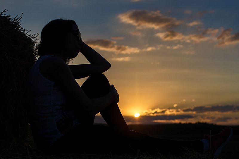 The shadow of a woman watching the sun set represents emotional recovery after caregiving ends.