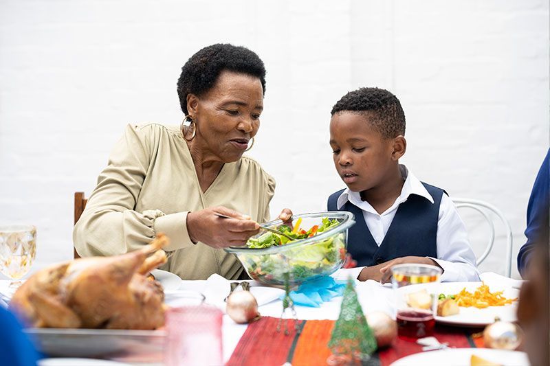 An older woman serves holiday food to her grandson, managing hypertension during the holidays with healthy choices.