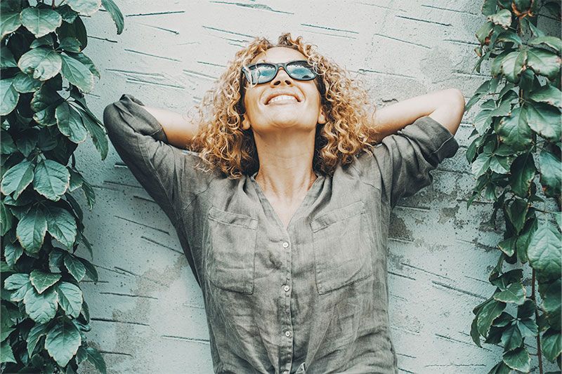 A woman wearing sunglasses relaxes with her arms behind her head, understanding the importance of building your emotional resilience as a caregiver.