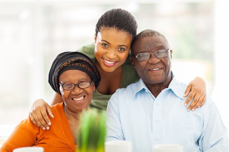 A woman caring for both aging parents gives them a hug.